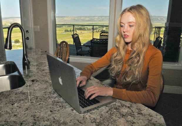 Plaintiff Sierra Norman sitting at a countertop looking at a laptop in a room with windows looking out to what looks like farmland