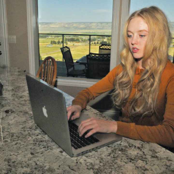 Plaintiff Sierra Norman sitting at a countertop looking at a laptop in a room with windows looking out to what looks like farmland